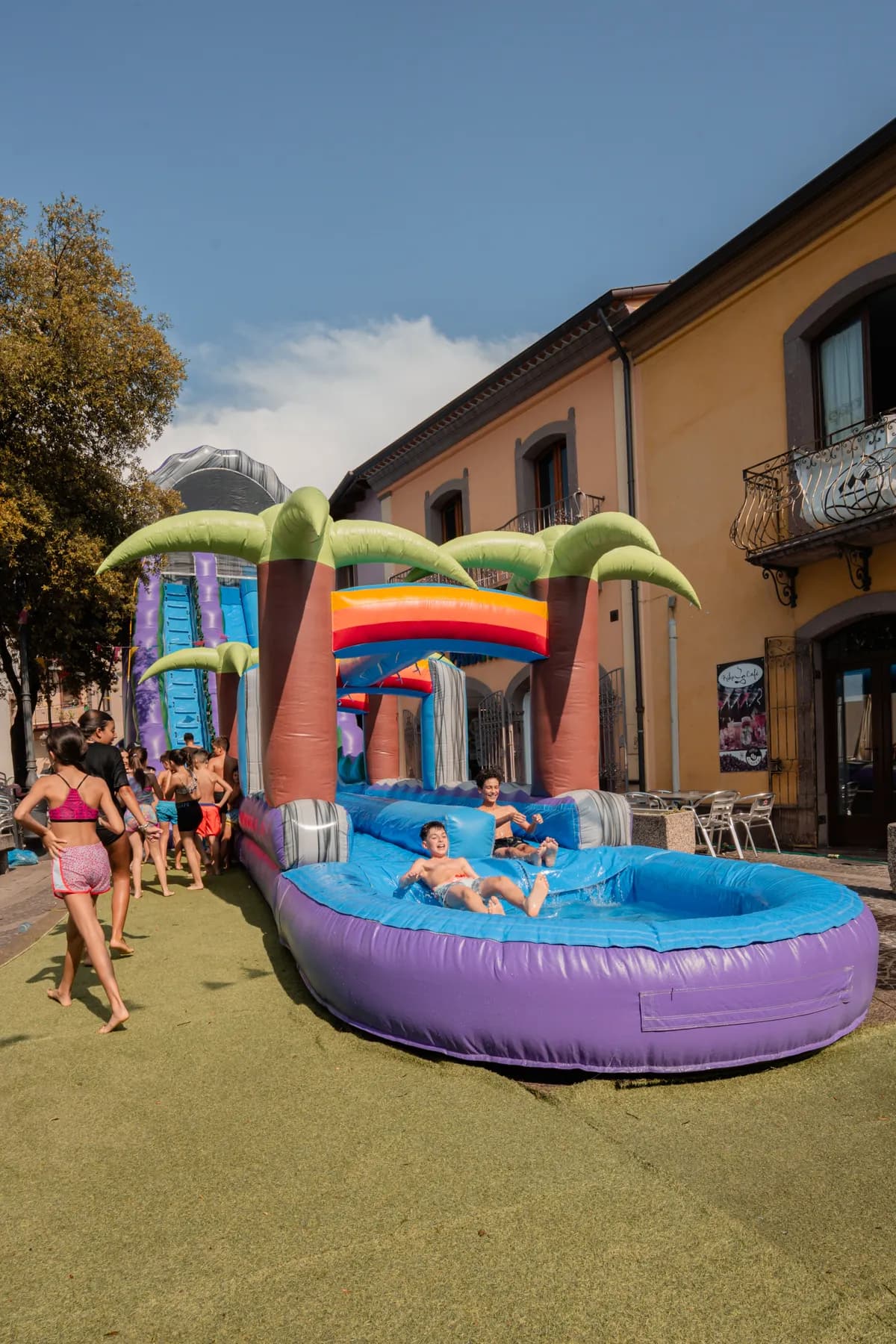 Ragazzi arrivano nella vasca del maxi scivolo acquatico con le palme, montato in piazza