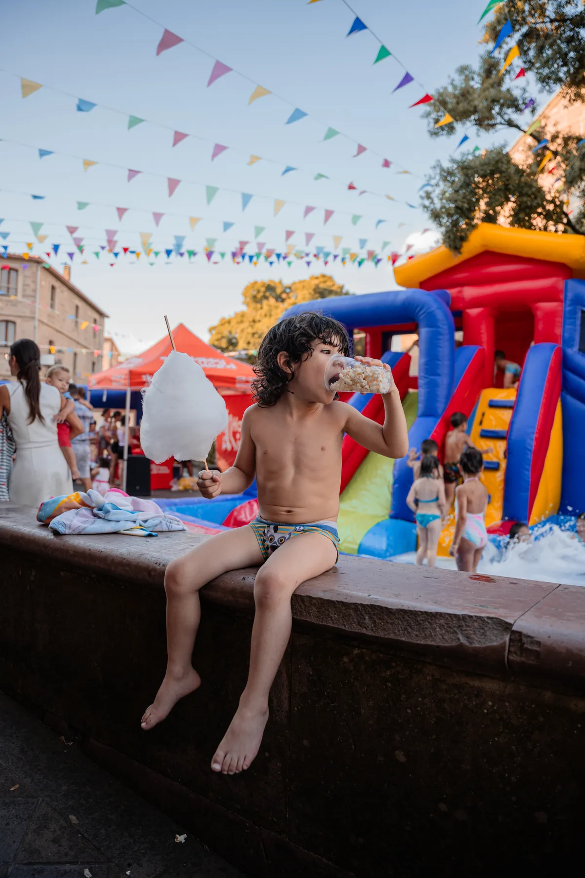 Bambino in costume da bagno con lo zucchero filato e il bicchiere di popcorn, davanti allo scivolo dell'Acqua Party