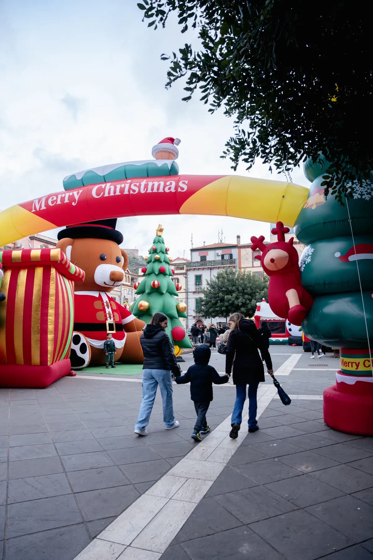 L'arco gonfiabile Merry Christmas del Villaggio di Natale in piazza, con orso e albero gonfiabili e famiglie in visita