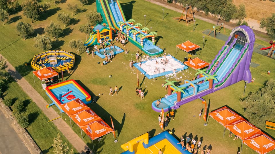 La stessa area durante l'Acqua Party: scivoli ad acqua, gonfiabili, gazebo arancioni e bambini che giocano