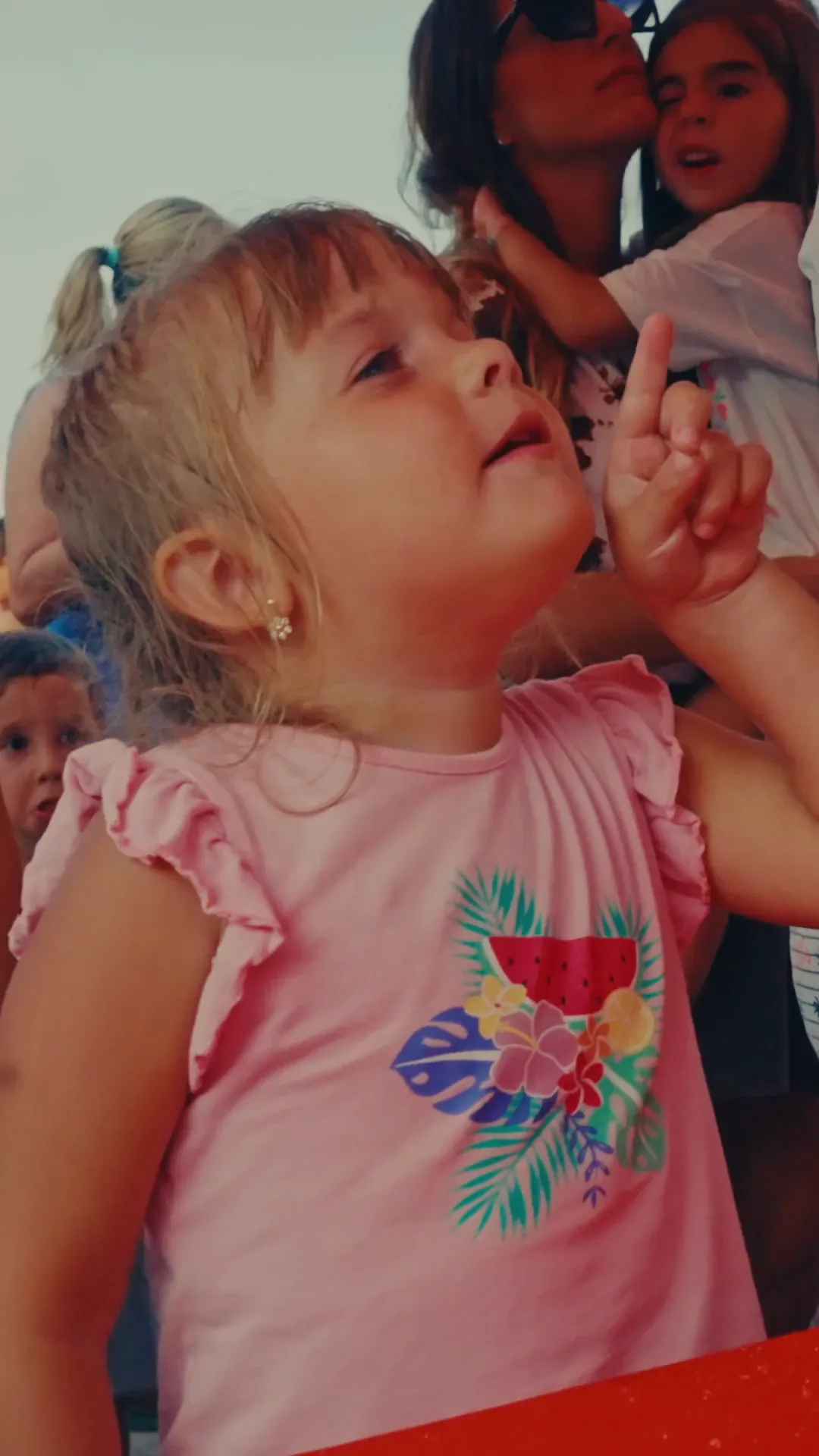 Bambina piccola col dito all'insù guarda le giostre del Luna Park