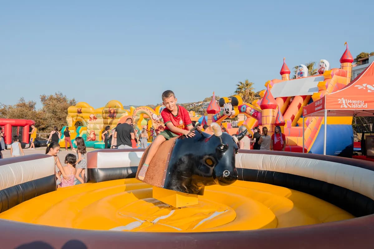 Bambino cavalca il toro meccanico al Luna Park, con castelli e scivoli gonfiabili alle spalle