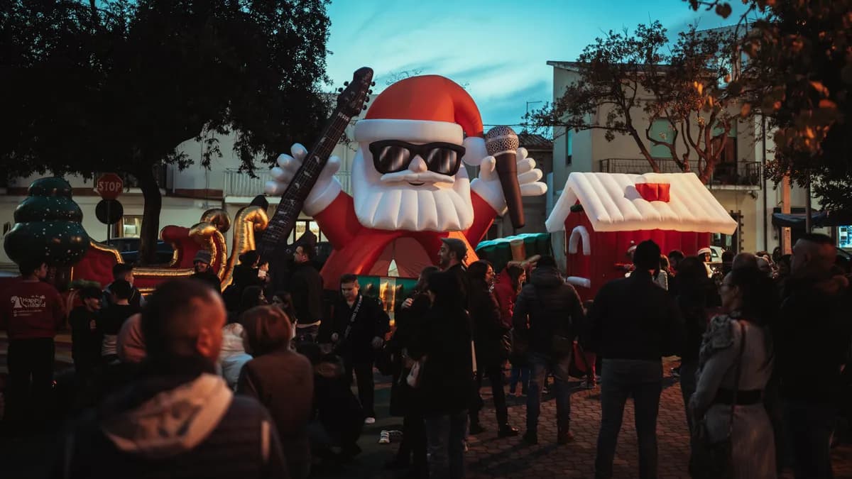 La casetta di Babbo Natale gonfiabile nella piazza al tramonto, accanto al Babbo Natale gigante