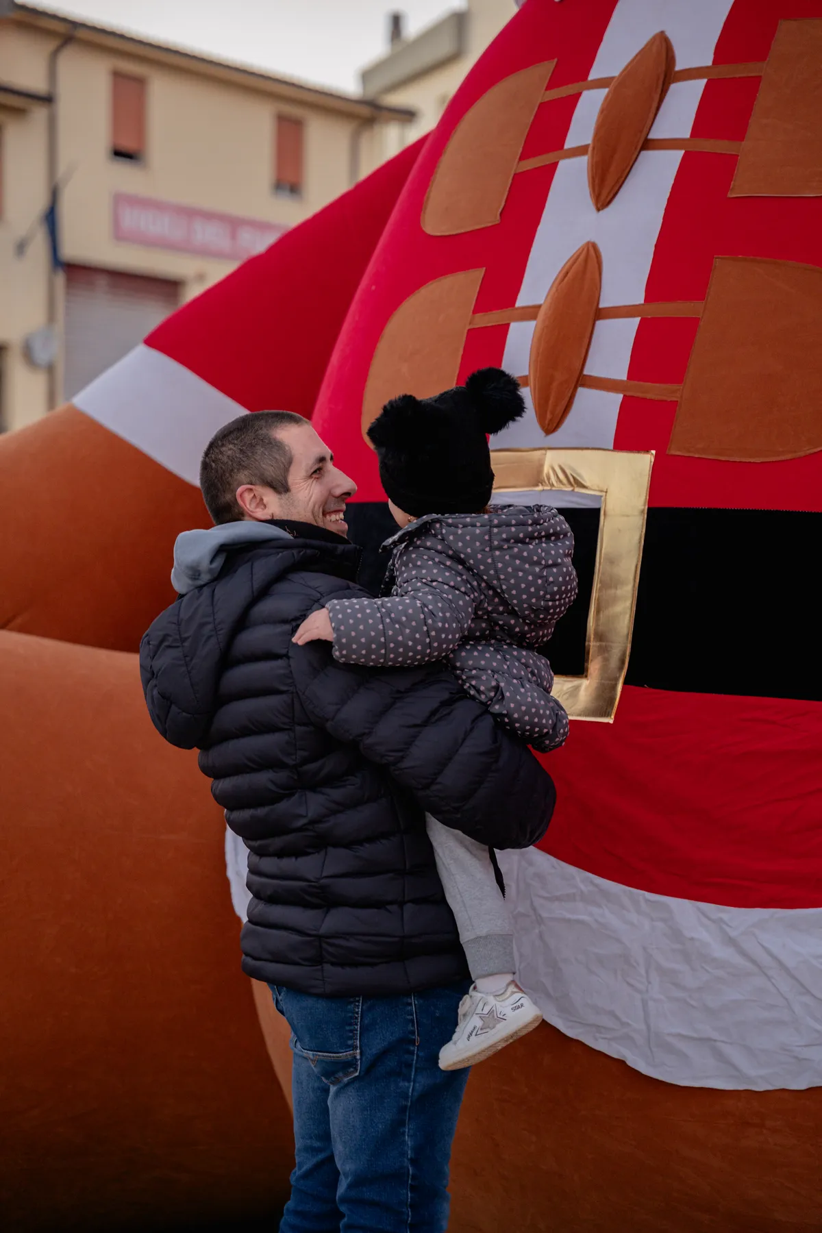 Papà solleva la figlia davanti alla cintura del Babbo Natale gigante