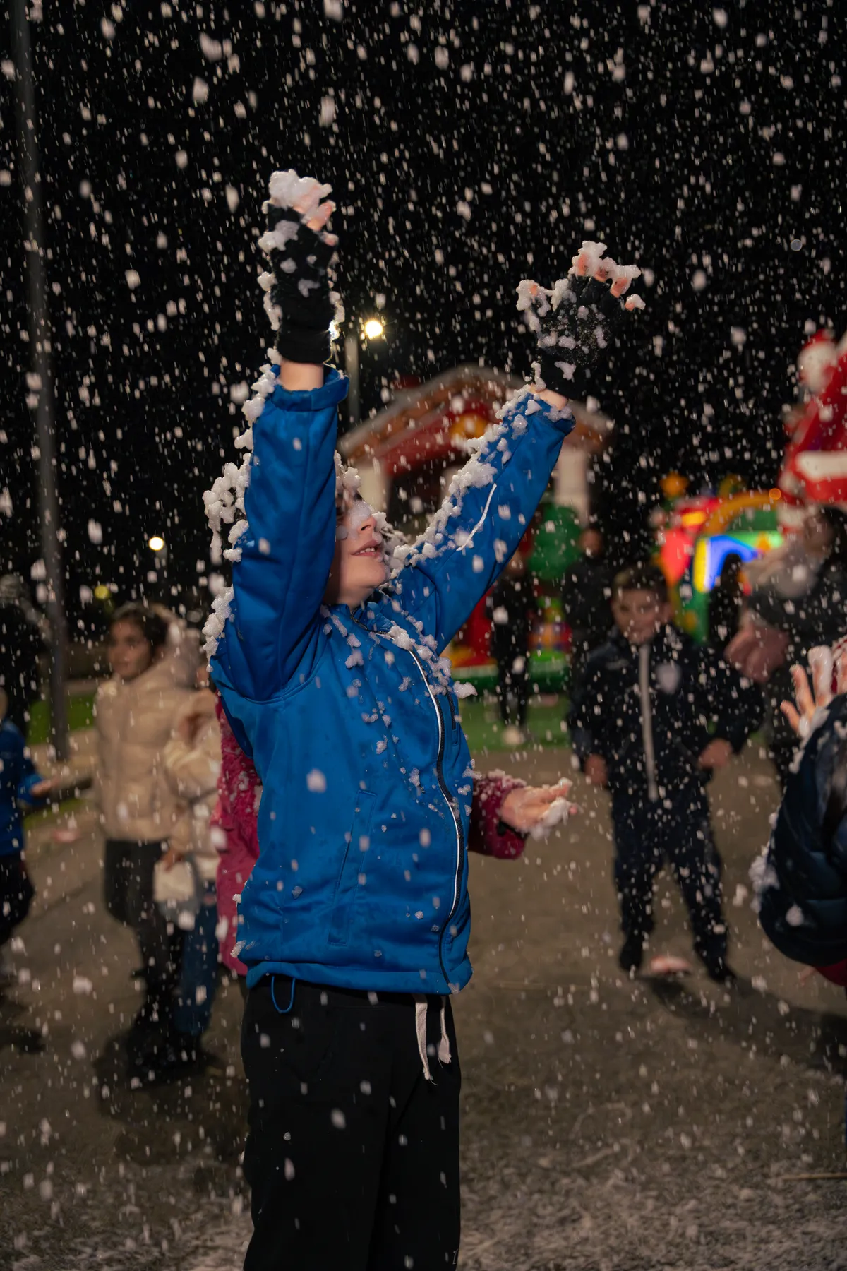 Ragazzo con le braccia al cielo sotto la nevicata del Villaggio di Natale