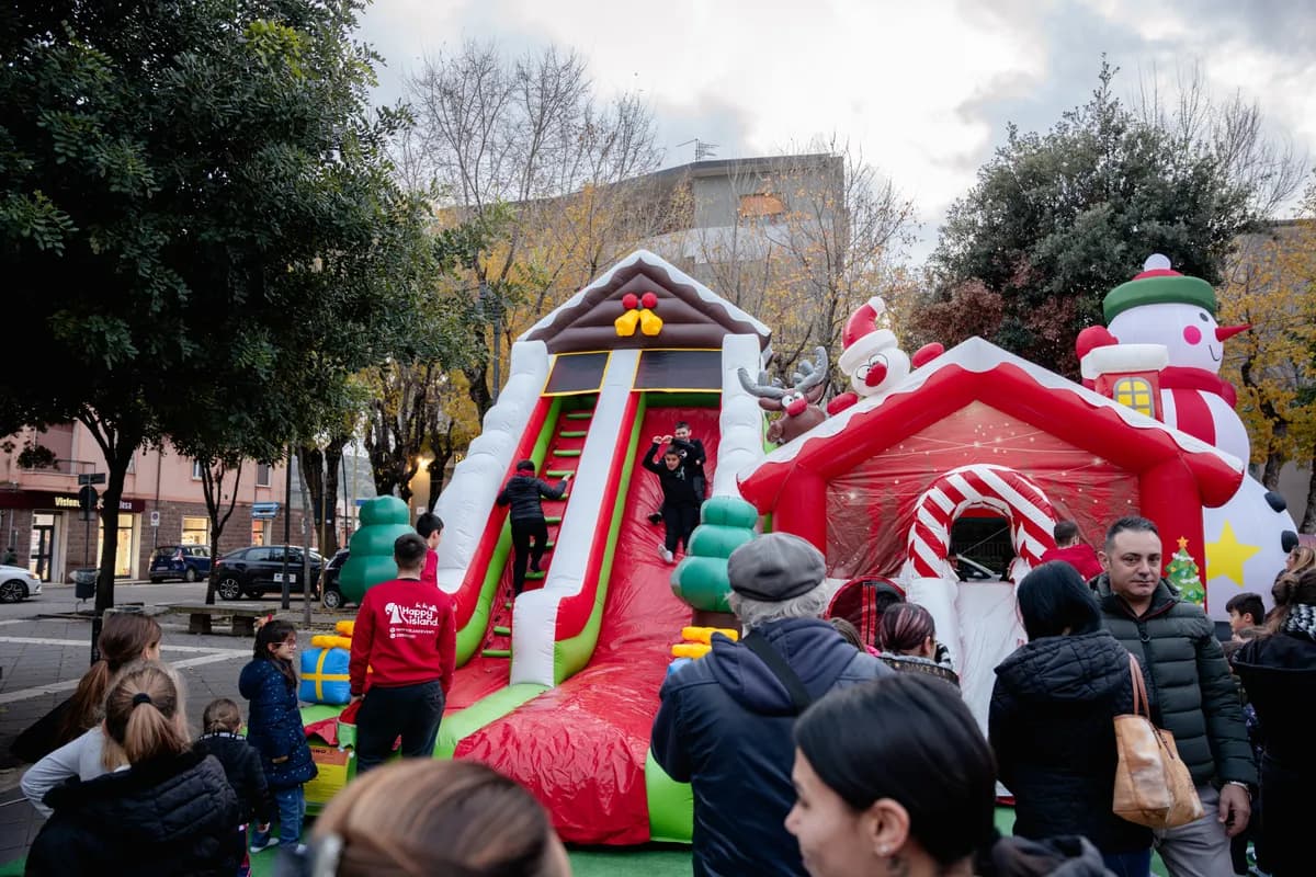 Bambini scendono dallo scivolone gonfiabile natalizio accanto alla casetta di Babbo Natale