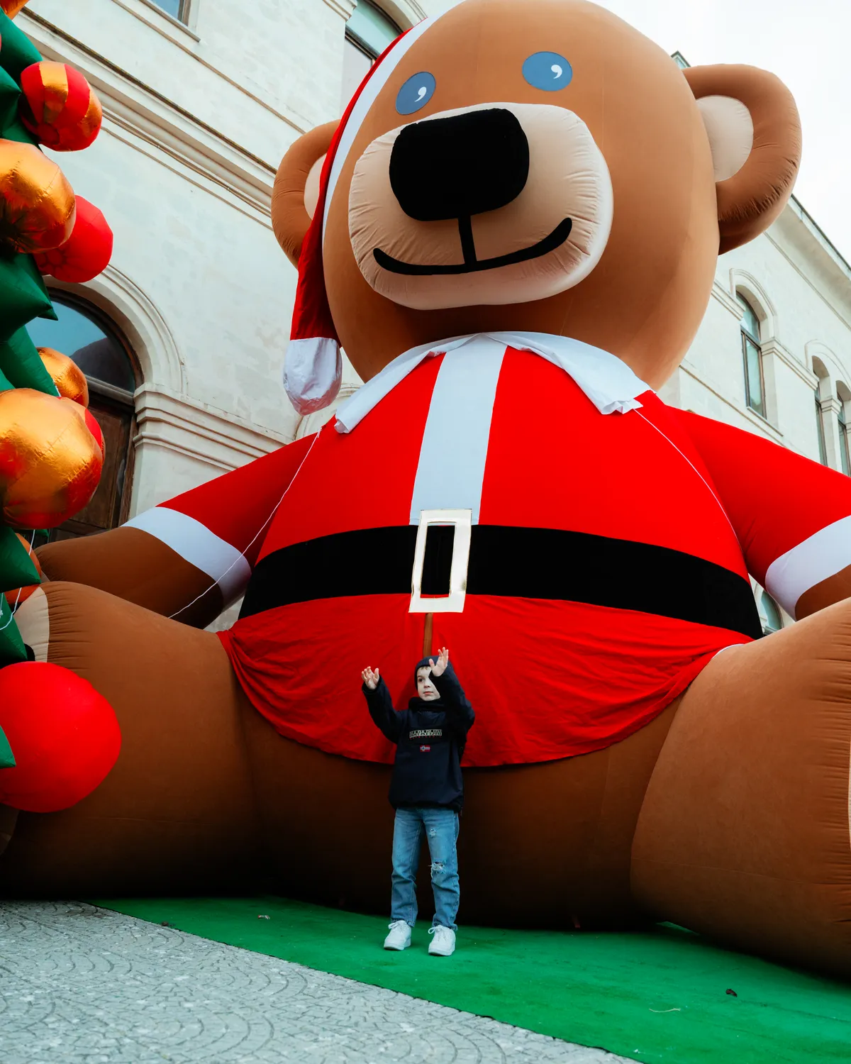 L'orso Teddy gigante vestito da Babbo Natale, con un bambino minuscolo alla sua base