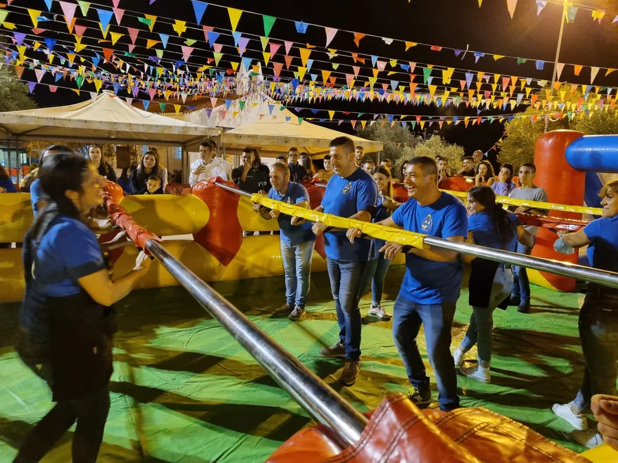 Adulti agganciati alle stanghe del biliardino umano durante una festa di paese in serata