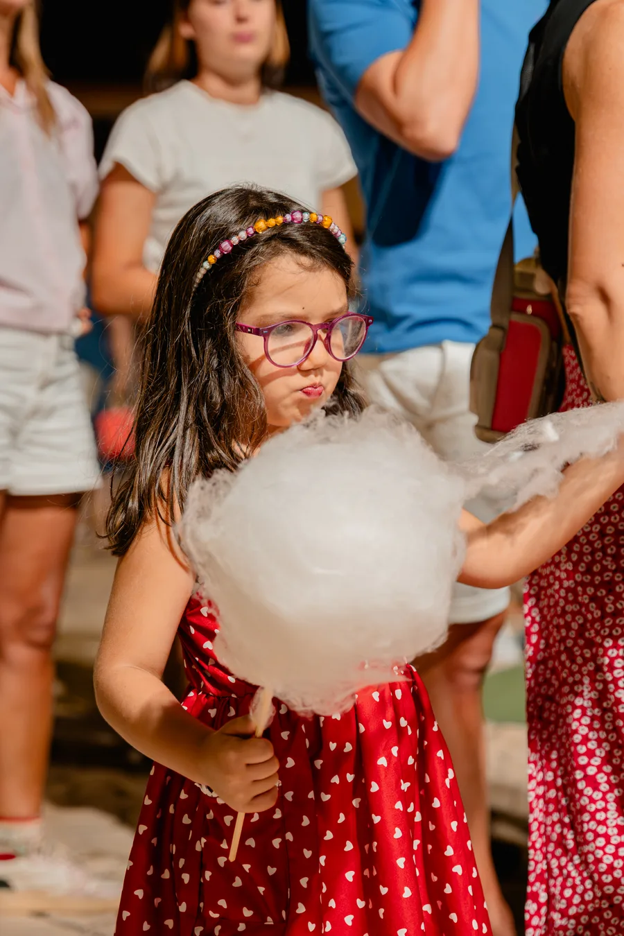 Bambina con un grande zucchero filato in mano, in mezzo alla gente a una festa d'estate