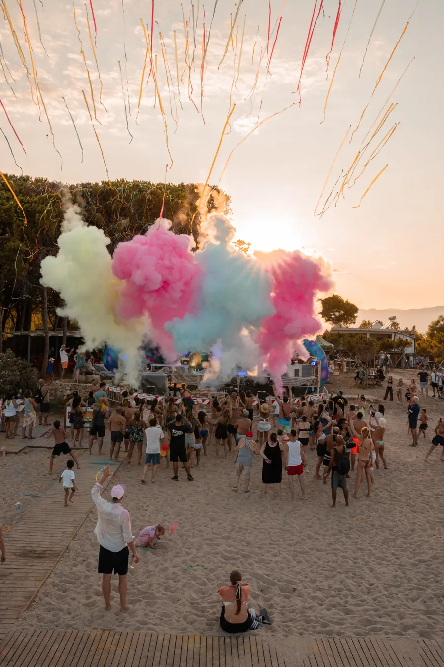 Nuvole di polvere colorata rosa e gialla sparate sul pubblico in spiaggia al tramonto