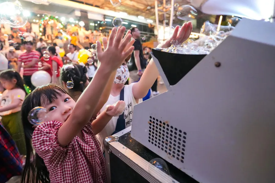 Bambina che allunga le mani verso le bolle sparate da una macchina professionale, in mezzo alla gente