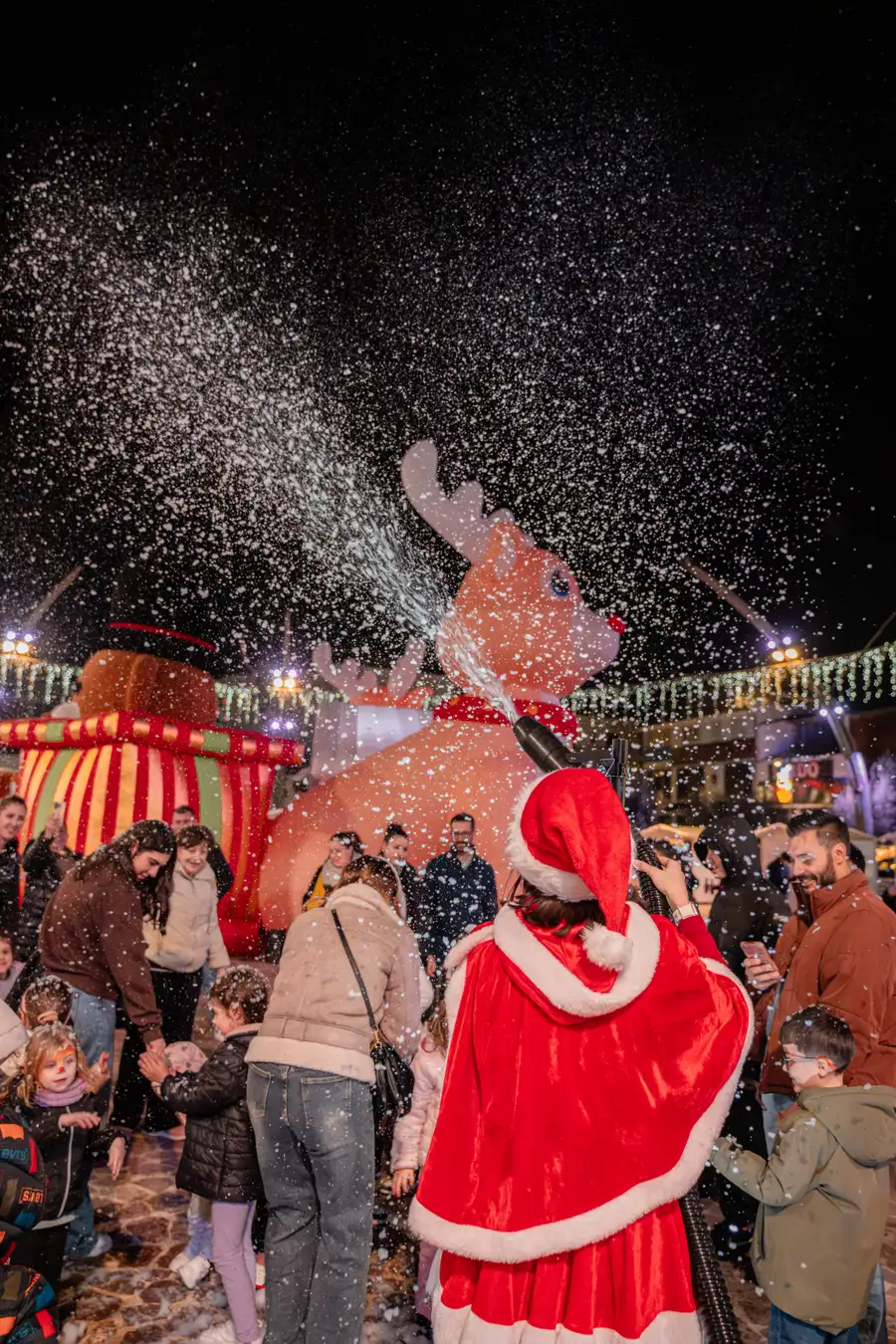 Cannone da neve che spara neve artificiale sulla piazza addobbata a Natale, con Babbo Natale in mezzo ai bambini