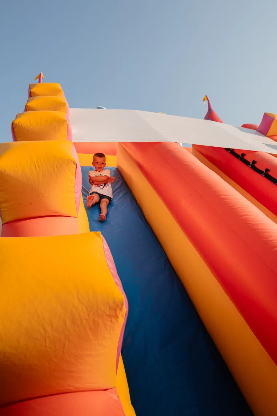 Bambino seduto in cima allo scivolo gonfiabile gigante arancione e blu