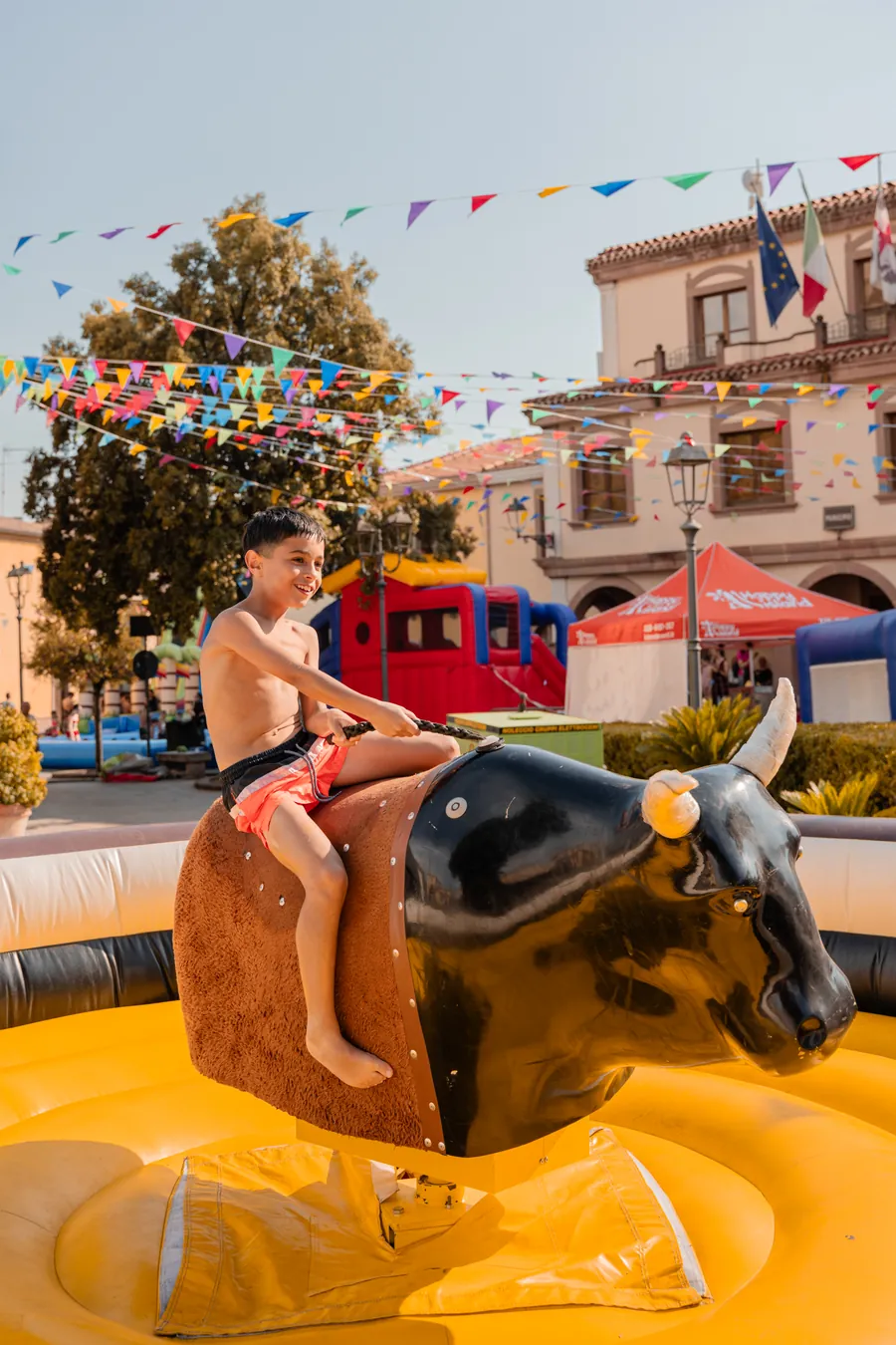 Ragazzo aggrappato al toro meccanico sul materasso gonfiabile, in piazza